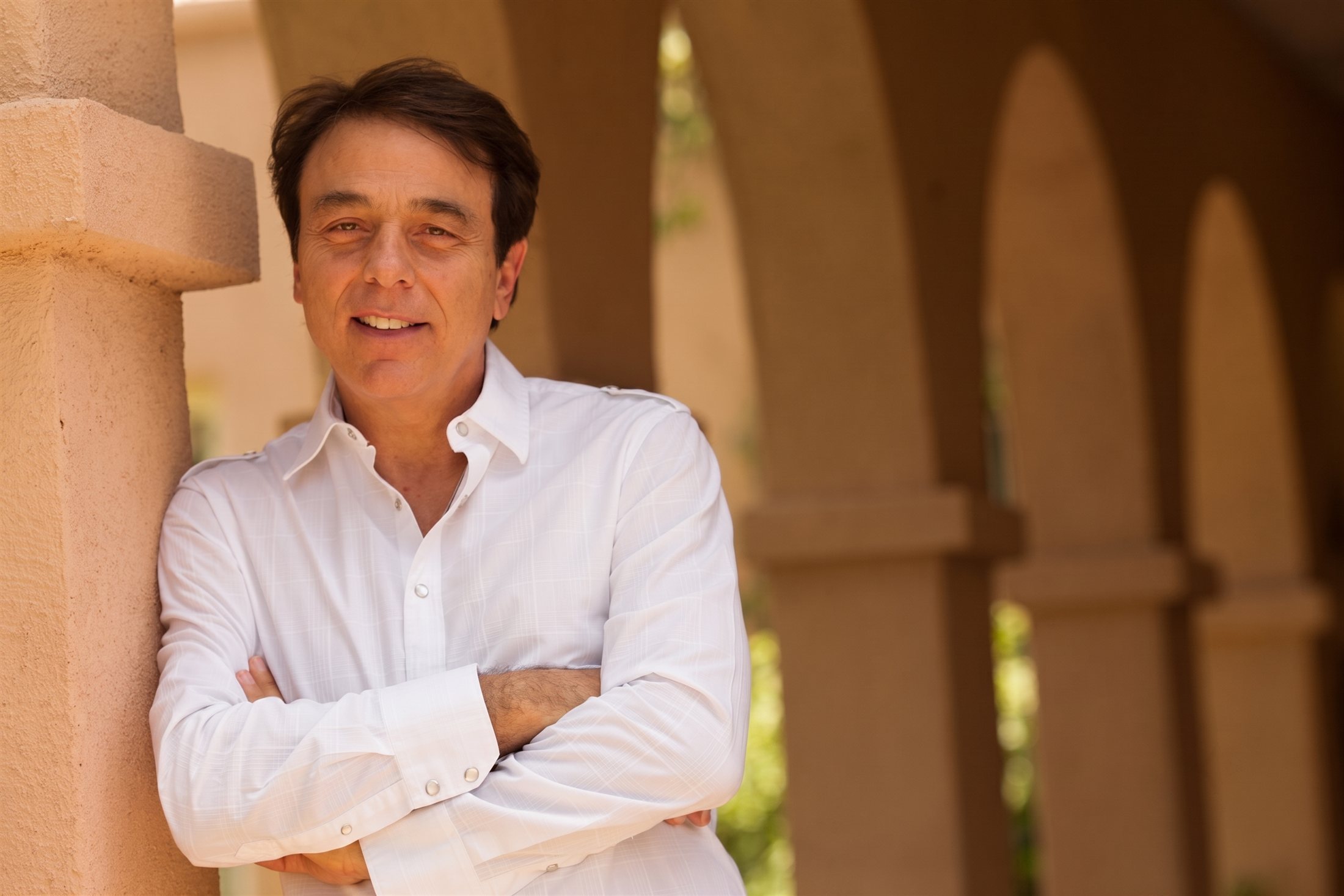 Dr. Thomas Lodi smiling with arms crossed, leaning on a stone column under desert archways